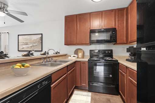Kitchen in 2 Bedroom California Place apartment with wood-style plank flooring, dark wood cabinetry, and black appliances. Plenty of storage space for all of your needs!