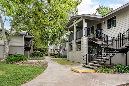 Charming exterior of Bent Tree Apartments with grass lined walkways, large trees, and quaint architectural details giving Bent Tree a homey and cozy feel like no other!