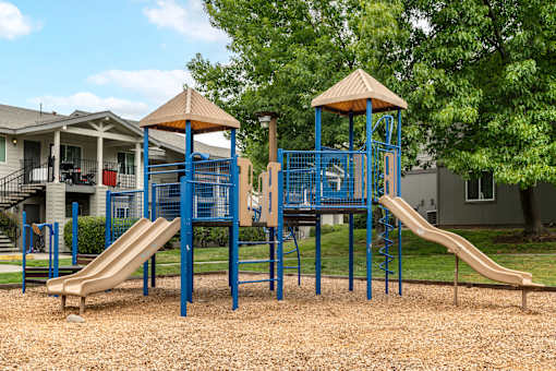 Play park at Bent Tree apartments with large play structure equipped with slides and climbing equipment. Surrounded by grass and cozy park-like landscaping