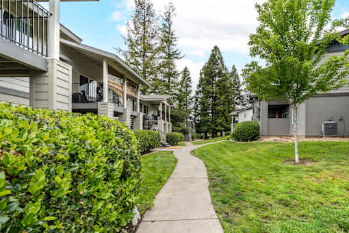 Charming exterior of Bent Tree Apartments with grass lined walkways, large trees, and quaint architectural details giving Bent Tree a homey and cozy feel like no other!