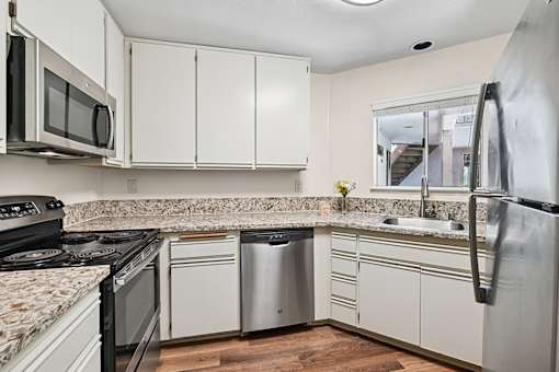 Kitchen in Cielo apartment home with plank flooring, updated appliances, and plenty of storage space. Charming window over kitchen sink overlooks serene courtyard with gorgeous landscaping.