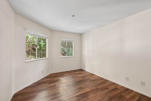 Spacious bedroom inside Cielo apartment home with plank flooring and large windows allowing for gorgeous natural lighting with views of trees
