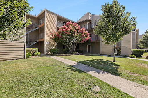 Charming exterior of California Place apartments with grass lined walkways and lush greenery, providing a beautiful and serene living experience!