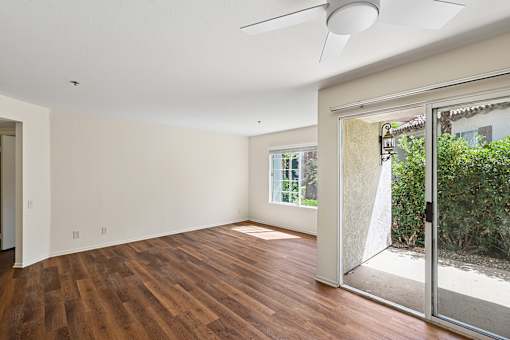 Spacious living area in Cielo apartment home with plank flooring, large windows, sliding glass doors leading to private patio and open concept layout leading to dining area and kitchen