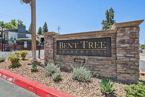 Entrance to Bent Tree Apartments with stone monument sign and large trees providing a cozy atmosphere