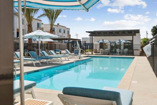 Swimming pool with striped umbrellas and sun loungers at Altitude Apartments, Moreno Valley, CA