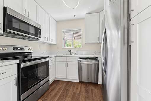 Updated kitchen in Cielo apartment home with plank flooring, white shaker cabinets, quartz countertops, updated appliances, and a charming window leading to courtyard.