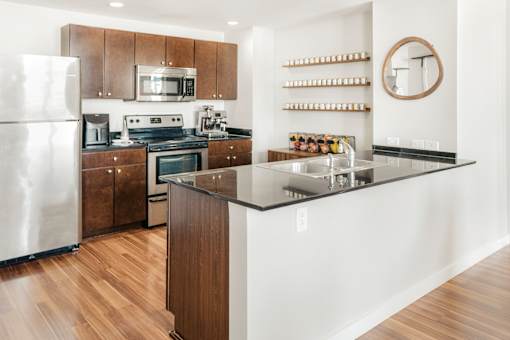 A modern kitchen with a refrigerator, microwave, oven, sink, and wooden cabinets.