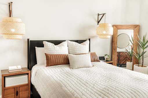 A bed with a white comforter and pillows is flanked by two hanging lamps.