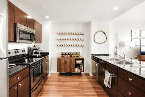 A modern kitchen with dark wood floors and stainless steel appliances.