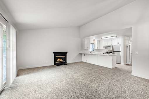 A living room with a fireplace and a kitchen in the background.