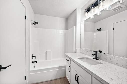 A white bathroom with a quartz countertop and a tub/shower.