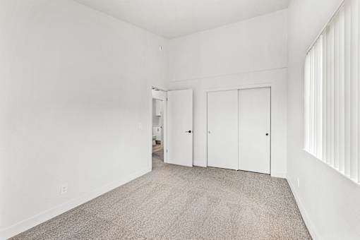 A room with white walls and carpeted floor with a doorway leading to another room.