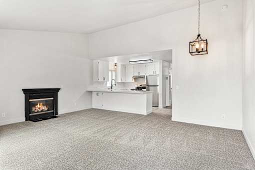 A living room with a fireplace and a kitchen in the background.