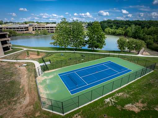 A tennis court is surrounded by a fence and a body of water. at The Residences at Tesson Ridge Apartments, Missouri, 63128