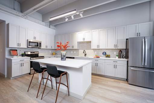 A kitchen with white cabinets and a white island with two black chairs. at The Residences at Tesson Ridge Apartments, Saint Louis