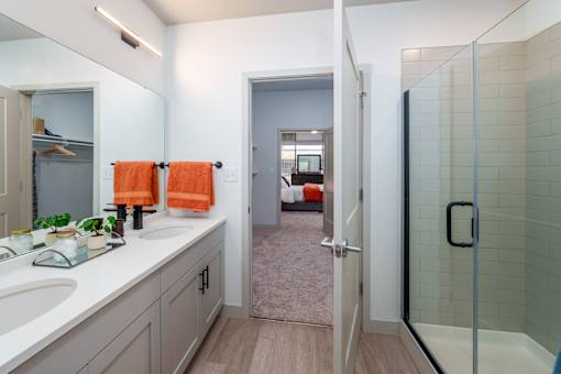 A bathroom with a walk-in shower and a vanity with two sinks. at The Residences at Tesson Ridge Apartments, Saint Louis