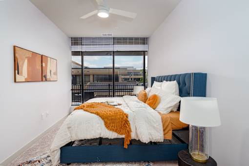 A bedroom with a bed, a lamp, and a painting on the wall. at The Residences at Tesson Ridge Apartments, Saint Louis, Missouri