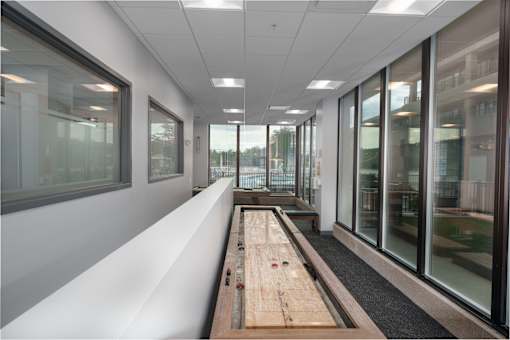 A long wooden table with a red object on it sits in a room with white walls and windows. at The Residences at Tesson Ridge Apartments, Missouri