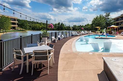 A poolside area with chairs and tables overlooking a pool. at The Residences at Tesson Ridge Apartments, Saint Louis, MO, 63128