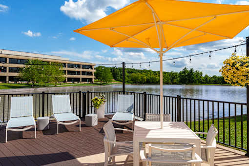 A yellow umbrella is on a patio table with chairs. at The Residences at Tesson Ridge Apartments, Saint Louis, Missouri