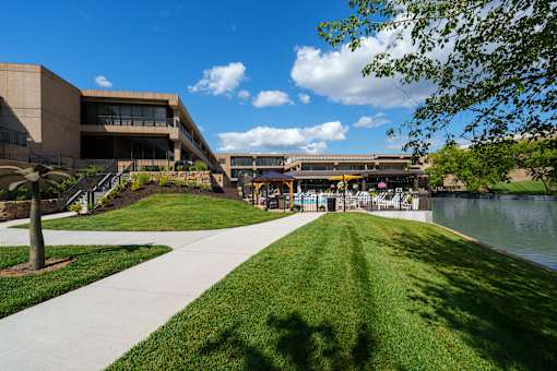 A walkway with a grassy area and a body of water in front of a building. at The Residences at Tesson Ridge Apartments, Missouri, 63128