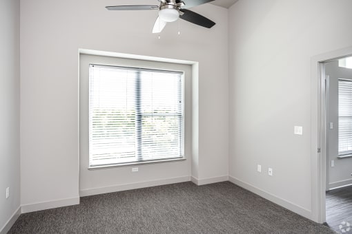 an empty bedroom with a large window and a ceiling fan