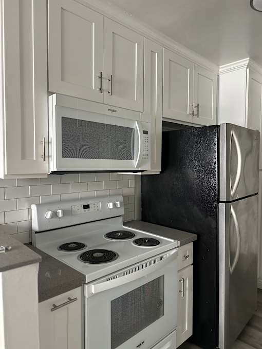 A black refrigerator is in a kitchen with white cabinets.