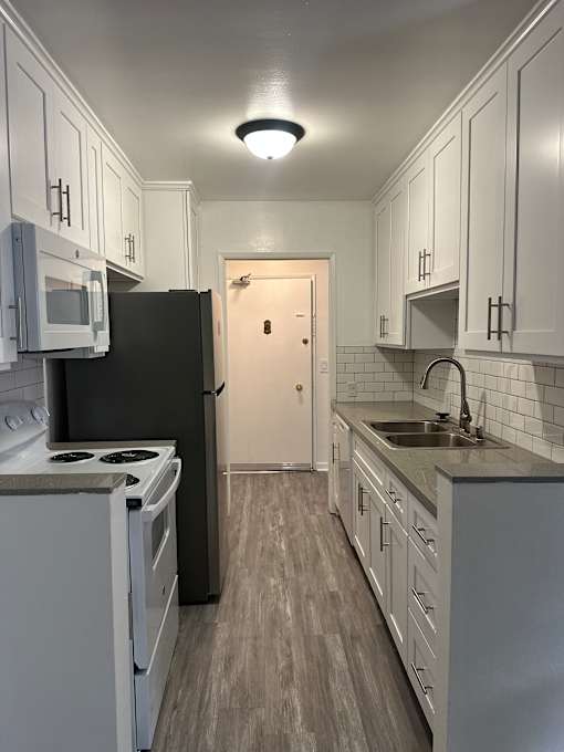A modern kitchen with a black fridge and white cabinets.