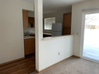 an empty living room with a kitchen in the background