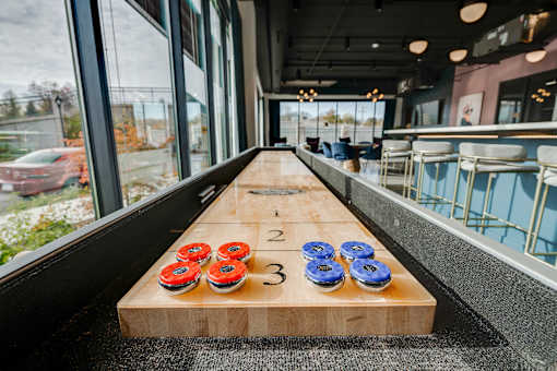 A tabletop shuffleboard indoor next to seating and a large window at The Shale, Minneapolis, MN