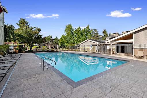 A swimming pool surrounded by a tiled patio and lounge chairs.