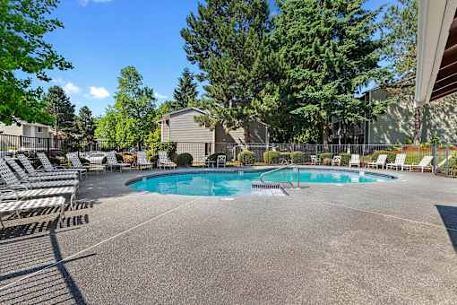 A large outdoor swimming pool surrounded by lounge chairs and trees.
