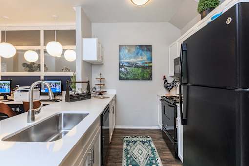 Churchill Estates, TX, Pet-Friendly Apartments - Apex Apartments - Kitchen With White Quartz Countertops, A Stainless Steel Sink, Black Appliances, and Pendant Lights.