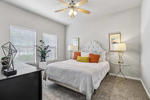 A bedroom with a bed, a ceiling fan, and a nightstand with a lamp.