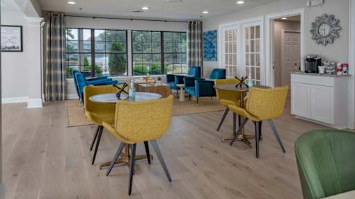 Apartments in Duluth, GA - Amberlake Village - Clubhouse With Colorful Seating, Large Windows, Wood-Style Flooring, And Coffee Station Near French Doors.