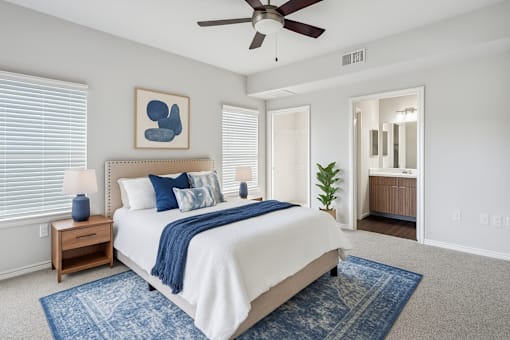 Northwest San Antonio, TX, Apartments for Rent - Azul Apartment Homes - Bedroom With Neutral Carpet, Ceiling Fan, Large Windows, Blue Area Rug, And Ensuite Bathroom.
