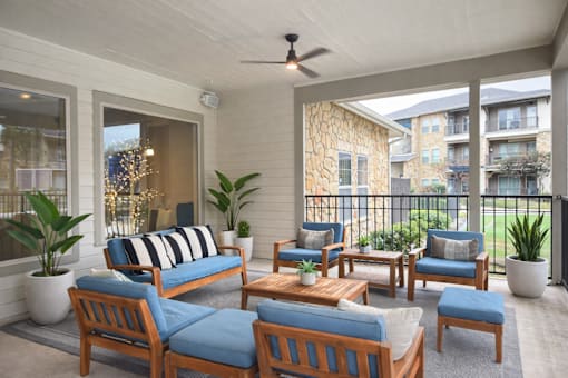 A patio with a blue cushioned sofa and wooden chairs.
