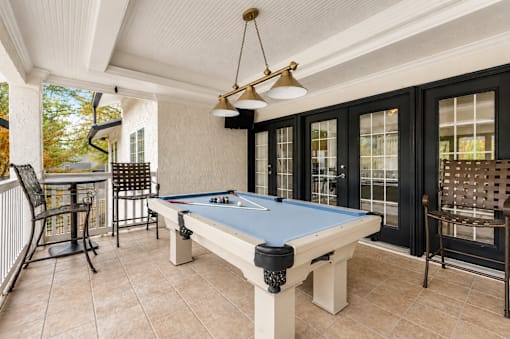 A pool table is in the middle of a room with a bar and chairs.