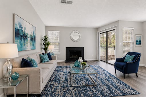 1-Bedroom Apartments in Sandy Springs, GA - Veridian at Sandy Springs - Living Room With A Beige Sofa, Blue Accent Chair, Fireplace, Glass Coffee Table, Large Area Rug, And Sliding Glass Door.