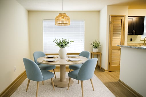 Townhomes in Duluth, GA - Amberlake Village - Dining Area With Round Table, Blue Chairs, Woven Pendant Light, Window Blinds, And Adjacent Kitchen Counter.