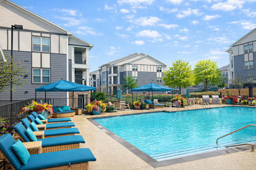 A swimming pool surrounded by lounge chairs and umbrellas in a residential area.