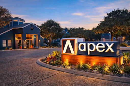 A large sign with the word "Apex" is lit up at dusk in front of a building.