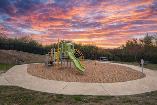 A playground with a green slide and a yellow and black swing set.
