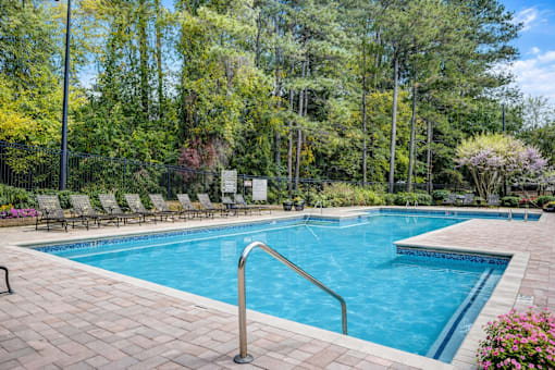 A large swimming pool surrounded by trees and chairs.