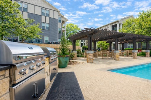 A modern outdoor kitchen with a grill and a pool.