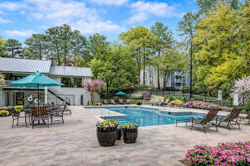 A pool surrounded by chairs and flowers with a house in the background.
