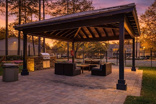 A pavilion with a stone floor and a roof is surrounded by trees.