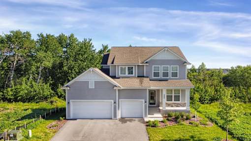 A two-story house with a garage is surrounded by greenery.