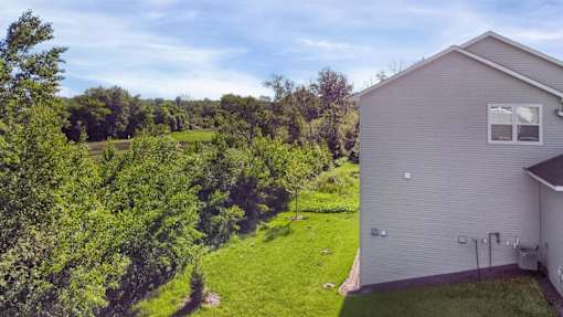 A house with a grey siding is surrounded by a green lawn and trees.